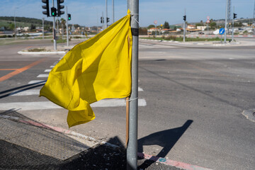 A bright yellow flag flutters on a pole at a traffic intersection in Israel, symbolizing hope for the safe return of hostages. The locality reflects ongoing tensions and community support.