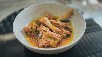 A close-up of a traditional spicy Indonesian chicken stew served in a white bowl.  