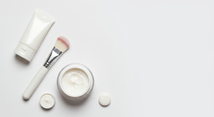 Fototapeta premium White cosmetic products arranged on a white background. A tube of cream, a makeup brush, and a jar of face cream are displayed, positioned in a flat lay style against a clean white surface.