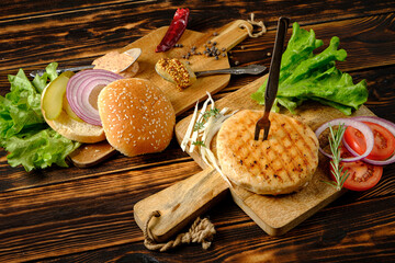 Juicy grilled chicken burger waiting to be assembled, surrounded by fresh veggies and herbs