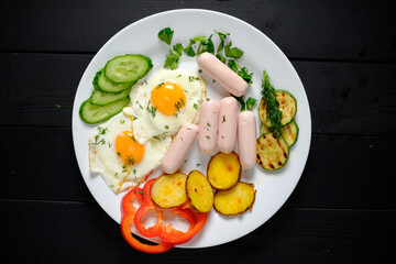 Savor a hearty breakfast with sunny-side-up eggs, sausages, and vibrant veggies on a sleek plate