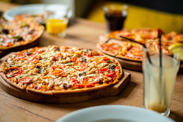 Mouth-watering pizzas with colorful toppings are served on a wooden table during a joyful gathering