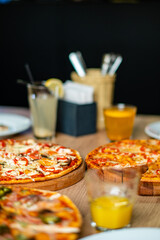 Colorful array of pizzas topped with various ingredients served alongside refreshing beverages