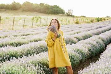 woman in yellow dress stands in lavender field, gently holding bouquet of lavender flowers. She appears serene and contemplative, enjoying beauty and fragrance of blossoms around her.
