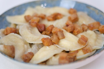 A platter of soft dumplings is served with crispy pieces of bacon on top. This hearty dish is perfect for a comforting meal, showcasing traditional flavors and textures.