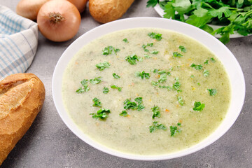 Homemade cream soup with chicken and herbs in a white plate on a gray background.