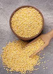 Millet groats in bowl and scoop on a gray background