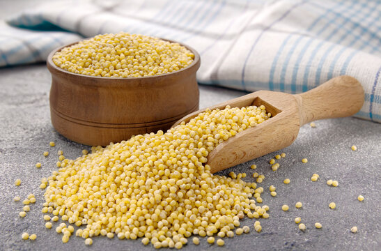 Millet groats in bowl and scoop on a gray background
