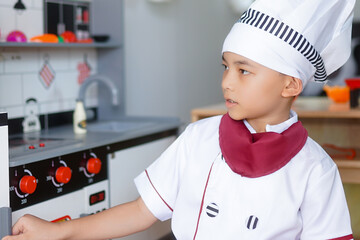 Little boy in chef hat and apron cooking in toy kitchen. Educational toys for young children. Kids play, portrait of Cute little Asian.playing at kitchen at indoor playground