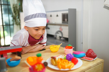 Little boy in chef hat and apron cooking in toy kitchen. Educational toys for young children. Kids play, portrait of Cute little Asian.playing at kitchen at indoor playground