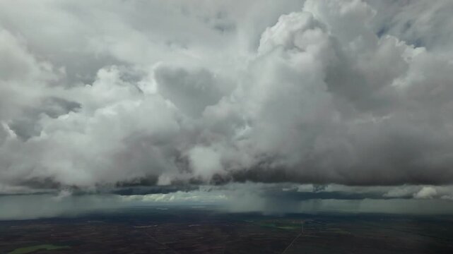 A pilot&rsquo;s view from inside an airplane cockpit flying through a stormy sky full of massive storm clouds with rainshowers over a plain in central Spain.