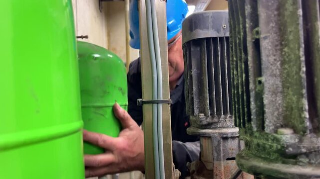 Closeup footage of a Caucasian worker uninstalling an expansion vessel in a factory setting