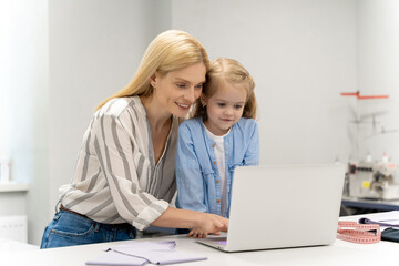 Obraz premium Mother tailoring a new model in her dress design studio, her daughter watching