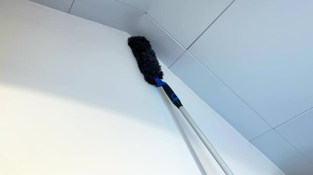 Close-up of a duster reaching a high ceiling corner with a telescopic pole in a clean interior.