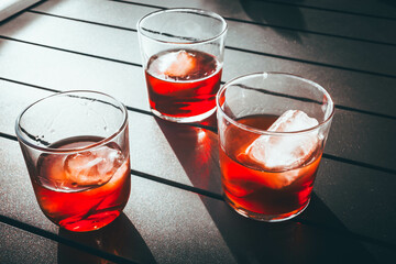 Three glasses of red vermouth with ice on a terrace table under sunlight