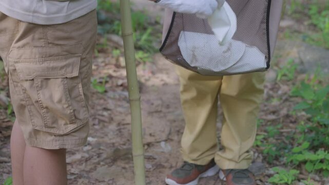 Slow motion shot of a person wearing a glove placing trash into a reusable bag during a forest cleanup, promoting eco-conscious habits, green living, sustainable trekking, and nature protection. - Powered by Adobe