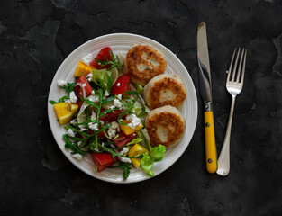 Potato tuna patties and fresh vegetable salad on a dark background, top view. Delicious lunch, dinner, brunch