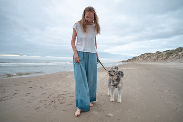 woman walking barefoot with her dog on beach of North sea, Denmark