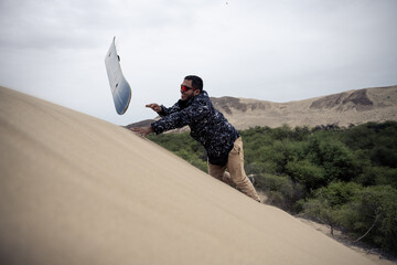 Smiling man tossing sandboard on dune, Cañoncillo, Peru