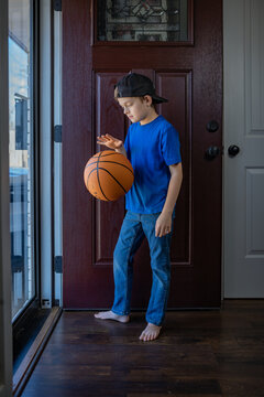 Boy bouncing basketball indoors near a wooden front door