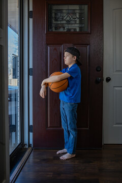 Boy in blue holding basketball, standing barefoot by door