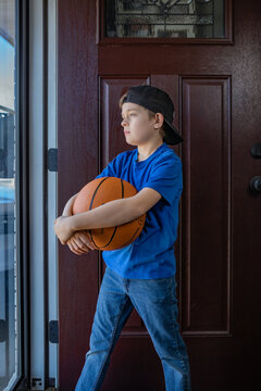 boy holding a basketball and staring out front door