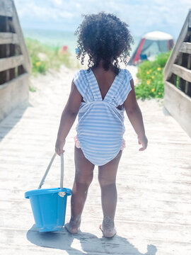 Young child with bucket strolls down to the sunny beach.