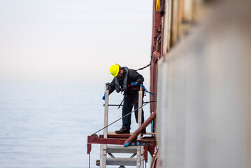 A deckhand prepares the pilot ladder as the ship readies for port entry. Secured in a safety...