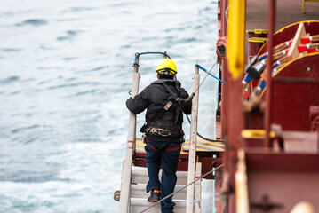 A deckhand prepares the pilot ladder as the ship readies for port entry. Secured in a safety...