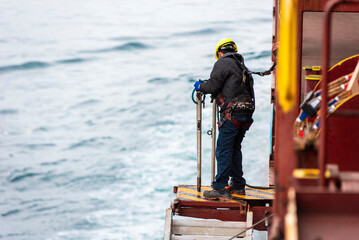 A deckhand prepares the pilot ladder as the ship readies for port entry. Secured in a safety...