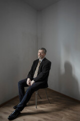 a man in a suit and tie sits on a chair in the corner of an old room