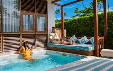 With palm trees swaying in the breeze, a digital nomad types on his laptop while a woman relaxes in...