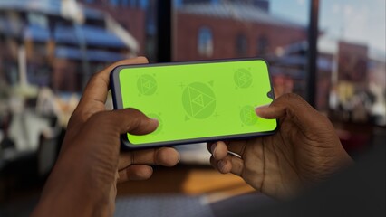 GREEN SCREEN CHROMA KEY A hand holding a smartphone in a bright cafe setting during the day. Perfect mockup for taxi, shopping, booking, or communication apps