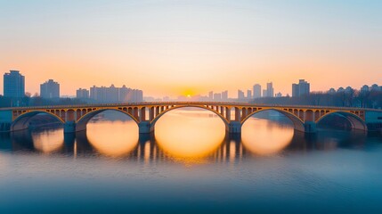 A stone arch bridge spans a calm river at sunrise, with city buildings silhouetted against a colorful sky reflected in the water.