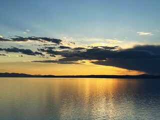 Obraz premium Serene sunset over tranquil lake reflecting golden sky and silhouette clouds