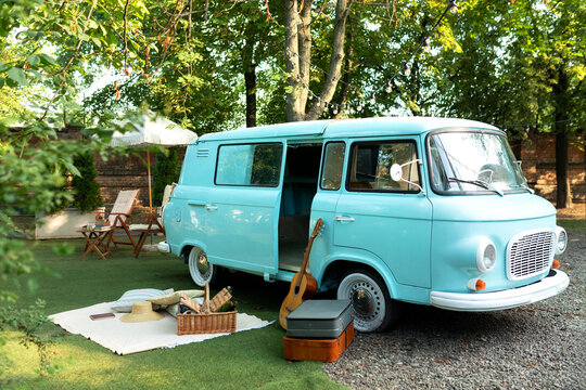 A place for relax nature with a picnic basket, plaid, guitar. Old vintage bus in garden. Blue classic Transporter retro vehicle with suitcases. Wedding auto decoration. Mint mini-bus in camping.	
