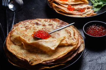 Pancakes with red caviar in a black plate close-up on the table. 