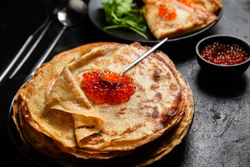 Pancakes with red caviar in a black plate close-up on the table. 