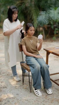 Asian mother braids her daughter's hair