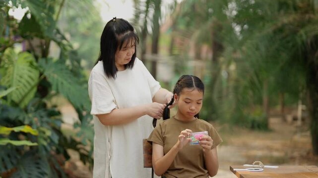Asian mother braids her daughter's hair