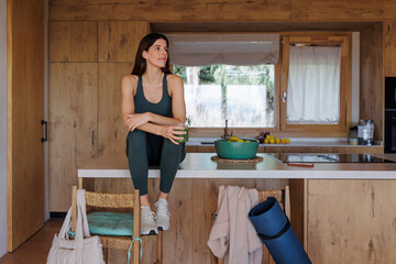 Woman sitting on kitchen counter with green juice in a sustainable home