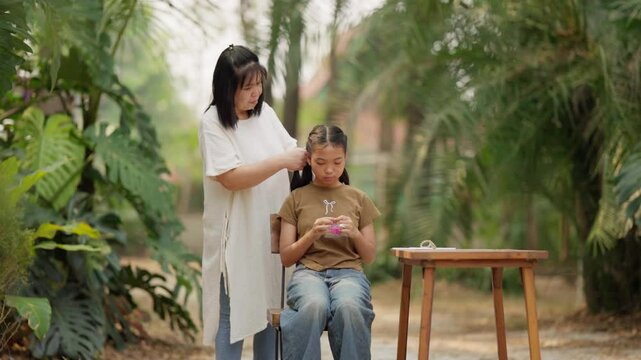 Asian mother braids her daughter's hair
