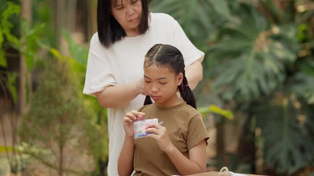 Asian mother braids her daughter's hair