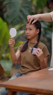 Asian mother braids her daughter's hair
