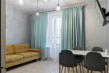 a large white dining table, grey chairs, a TV, grey walls, a white door. The design of a simple dining room or kitchen. The dining area.