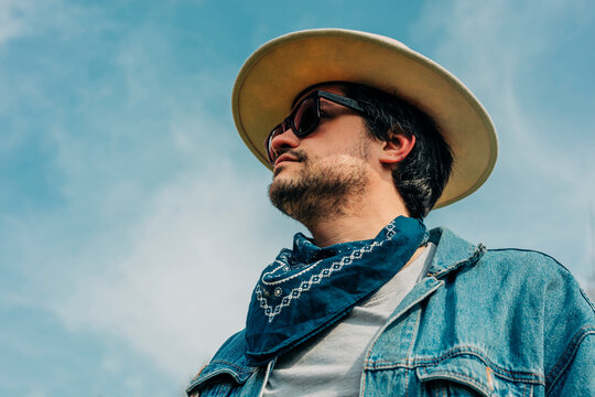 Stylish man in denim and hat looking away under blue sky