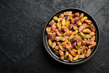 Pistachios. Black stone bowl with peeled roasted pistachio kernels. Close-up on a black stone background.