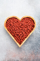 Heart-shaped bowl with dry cat food. On a gray concrete background. Top view.