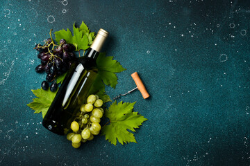 White Bottles of wine, bunch of grapes, glasses, corkscrew and corks on dark textured table. Top...
