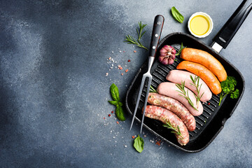 Pan with raw meat colored sausages. On a stone dark background. Top view. Free space for text.
